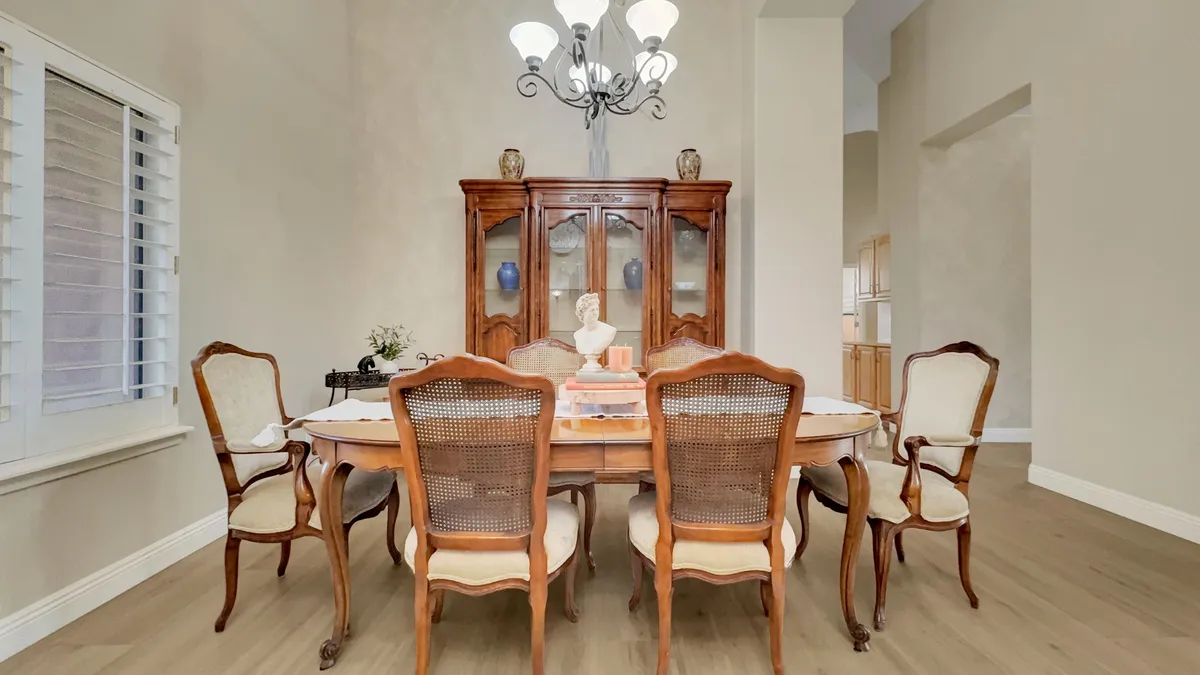 An elegant formal dining room with a large table set for eight, a china cabinet, chandelier, and tasteful decorative accents. The mood is sophisticated yet warm, inviting memorable gatherings and celebrations.