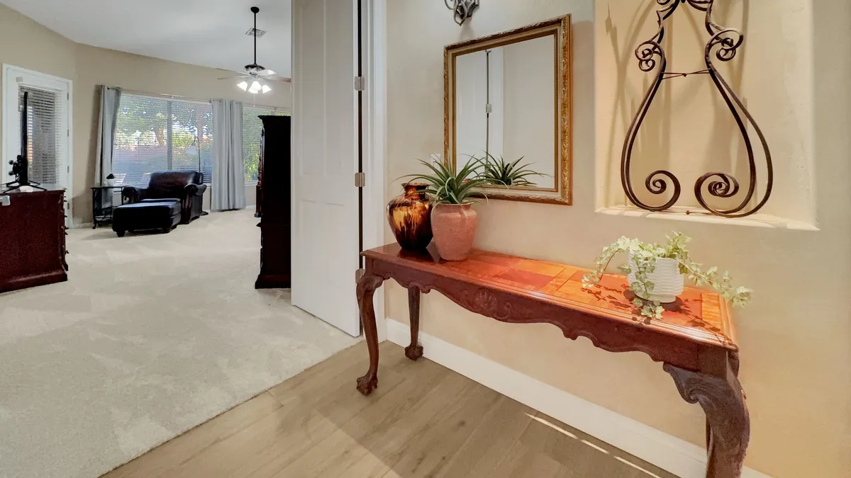 A stylish entryway featuring a decorative table, mirror, and lush indoor plants, with a glimpse into an adjacent, welcoming living area. The space is bright and inviting, setting a warm first impression for guests arriving at the home.