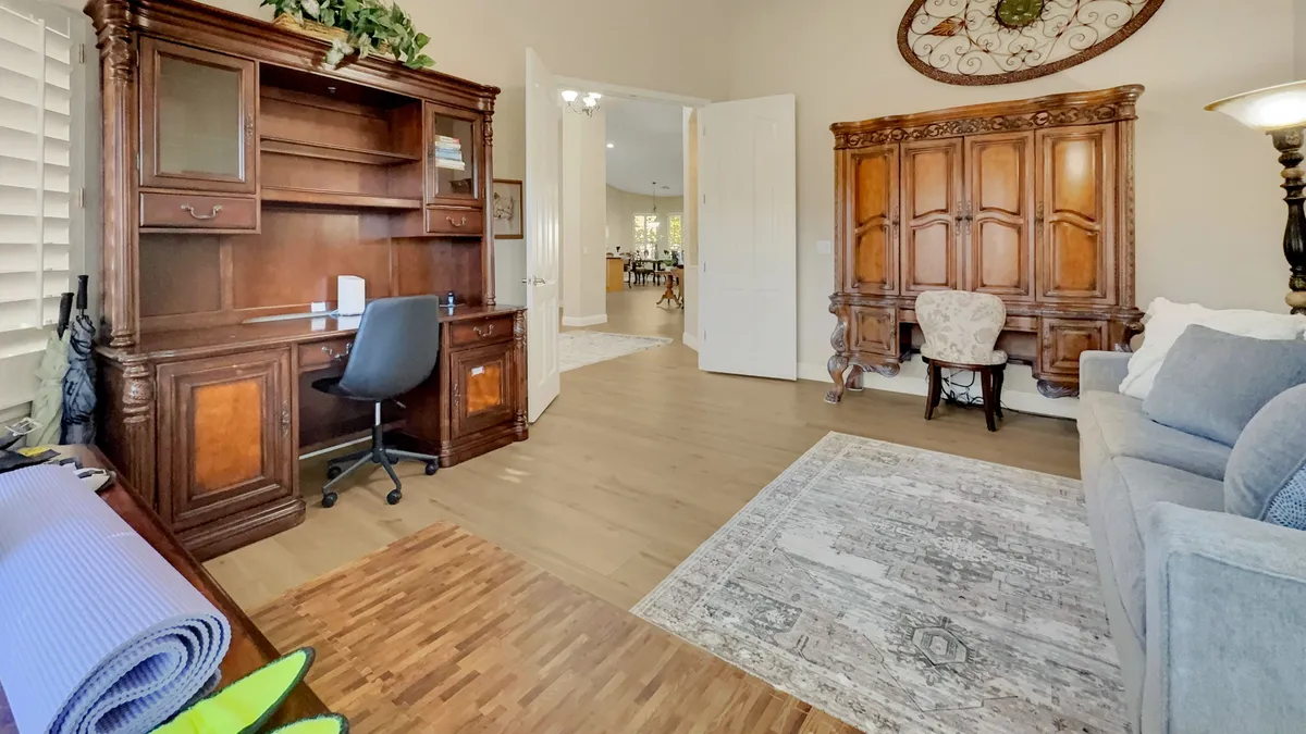 A quiet, productive office setup featuring a wooden desk and chair, antique cabinet, sofa, and area rug—bathed in calm, neutral tones for a peaceful work environment.