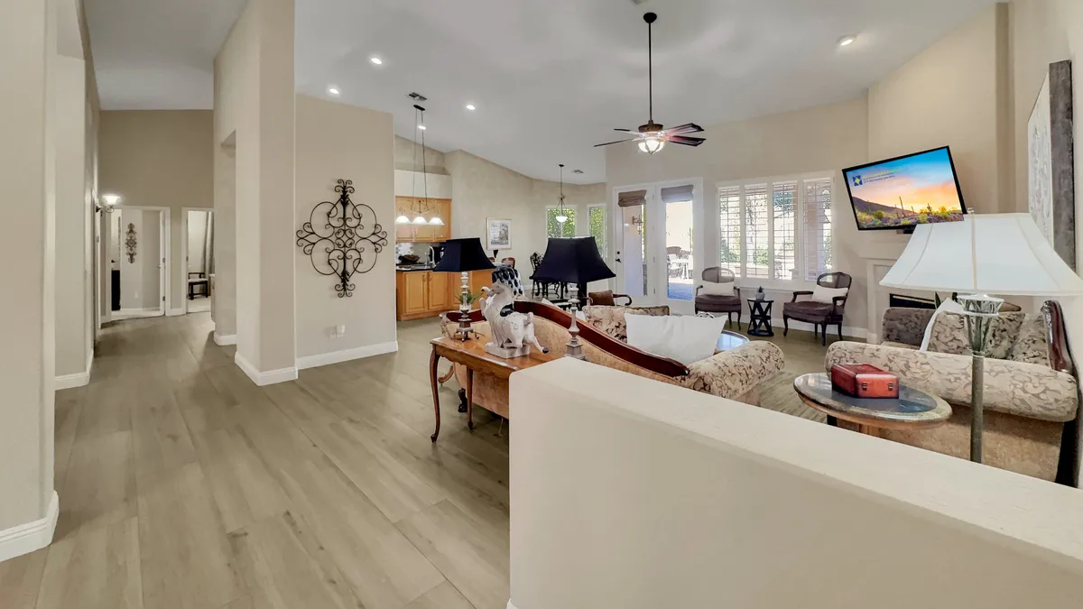 A cozy living room with a comfortable sofa, coffee table, television, ceiling fan, and large windows allowing natural light to flood the space. The layout invites socializing or relaxation after a busy day.