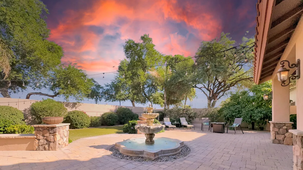An inviting exterior seating area sits beside a tranquil fountain, surrounded by mature greenery. The setup suggests a peaceful spot for sunset watching, casual conversations, or reading—a perfect complement to the active lifestyle of golf enthusiasts.