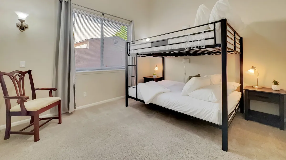 A welcoming bunk room with a queen-over-queen bunk bed, nightstand with lamp, and a chair by the window. The space exudes warmth and is perfect for children or cousins to share stories and laughter.