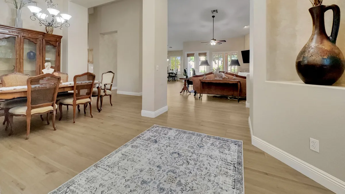 A wide, inviting view of an open-concept living and dining area. A chandelier sparkles above a large dining table set for a gathering, with a plush sofa and decorative rug in the background. Sophisticated décor and a large decorative vase add classic Venetian touches.