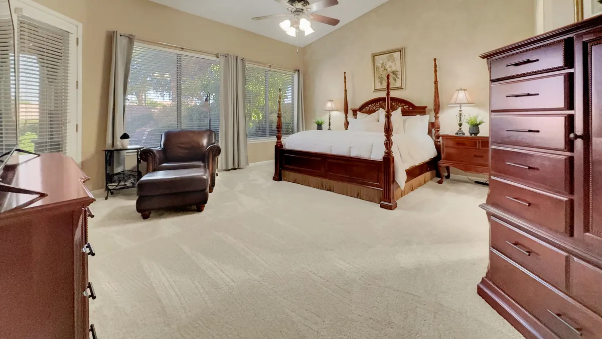 A serene bedroom featuring a four-poster bed, leather armchair, and dresser. Soft natural light streams in, illuminating plush bedding and tranquil decor that create an inviting atmosphere for relaxation or reading.